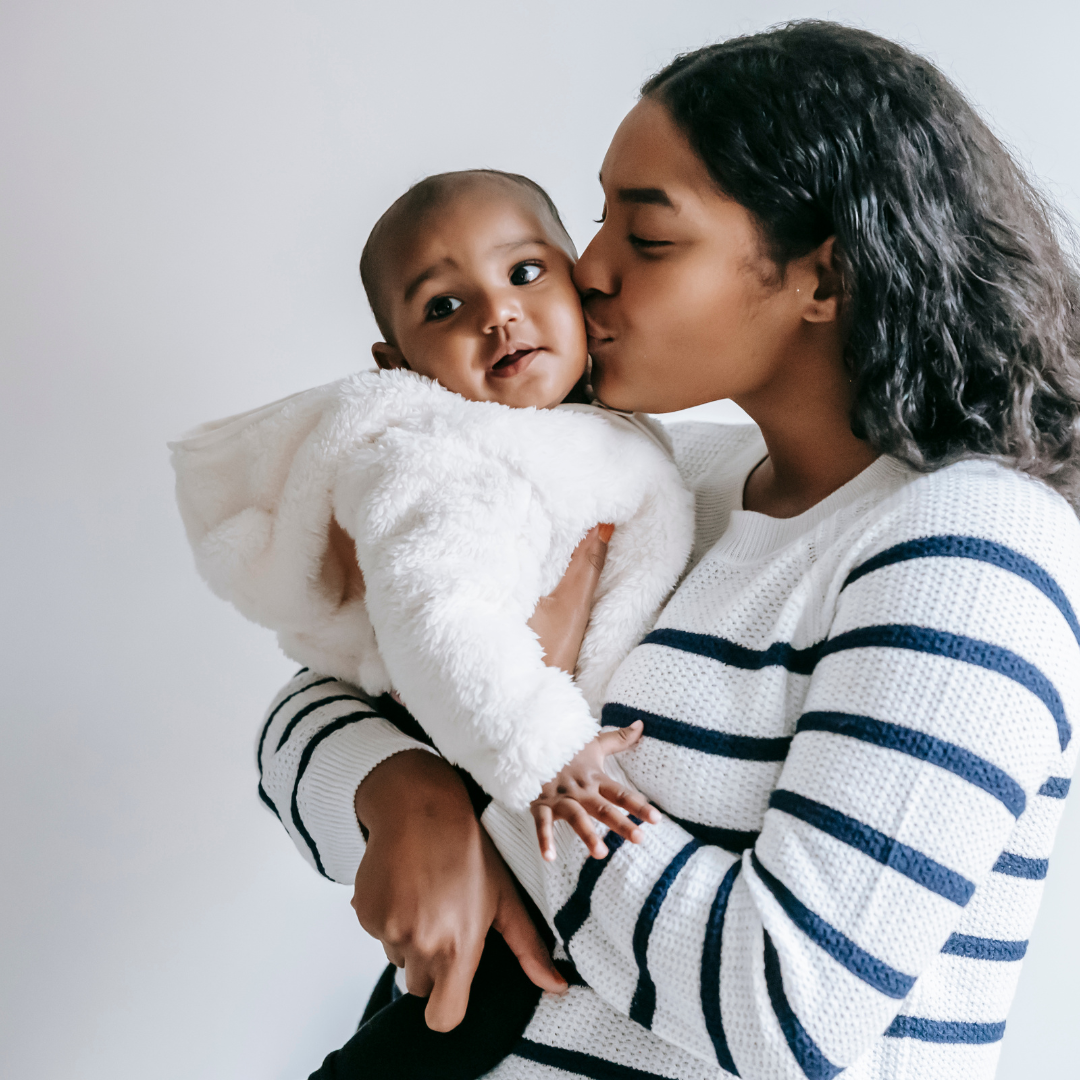 A mom is pictured kissing her baby on the cheek