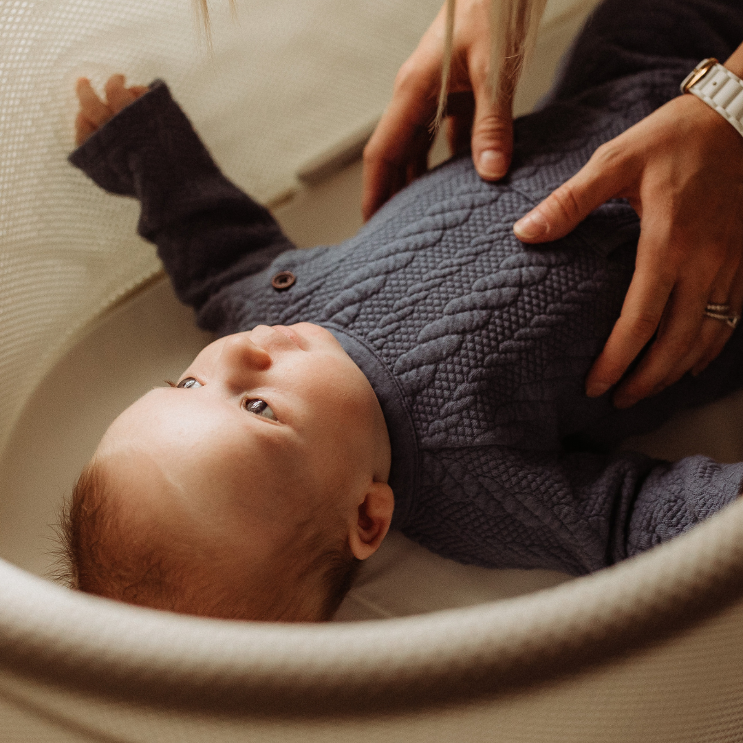 A mom is gently placing her baby into his crib