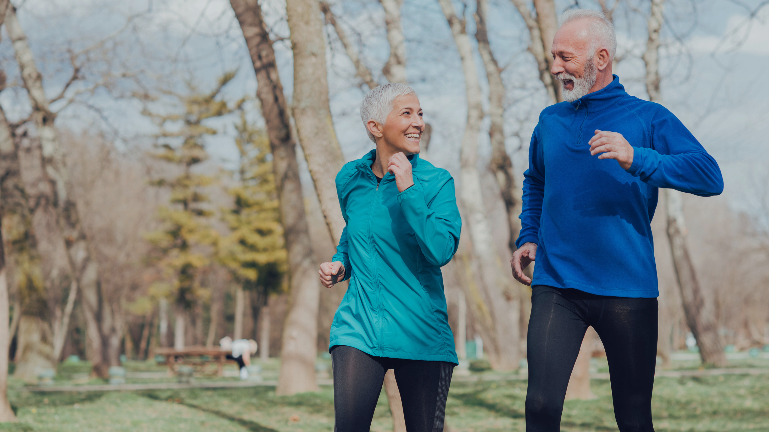 An older couple is pictured lightly jogging outside together, smiling and being active