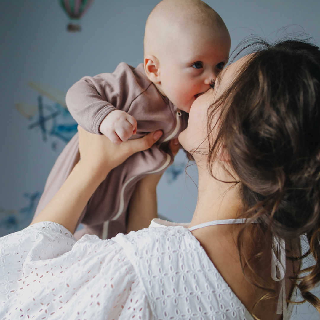 A mom is seen holding and lifting her newborn infant while smiling