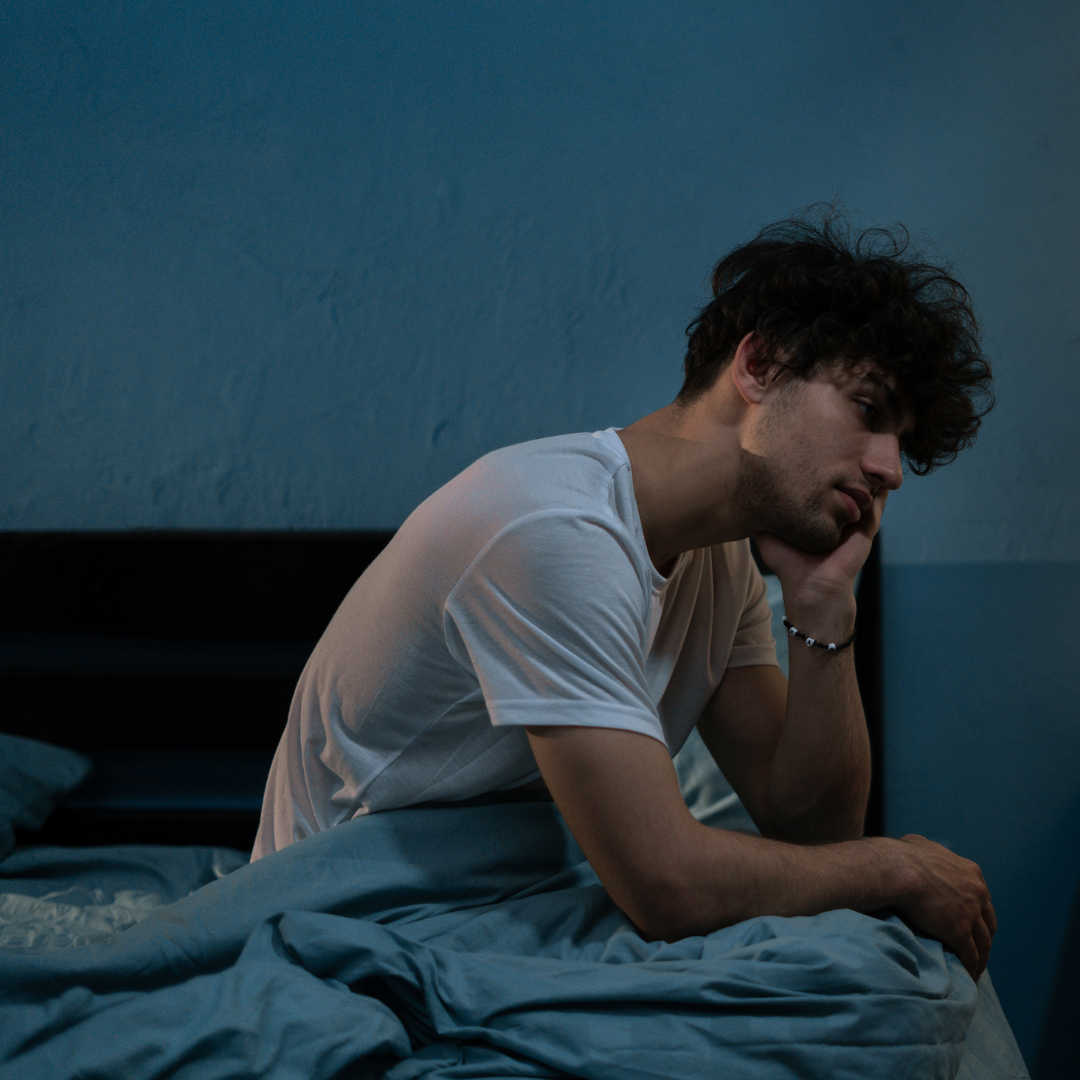 a Man is shown sitting up in bed late at night and looking restless