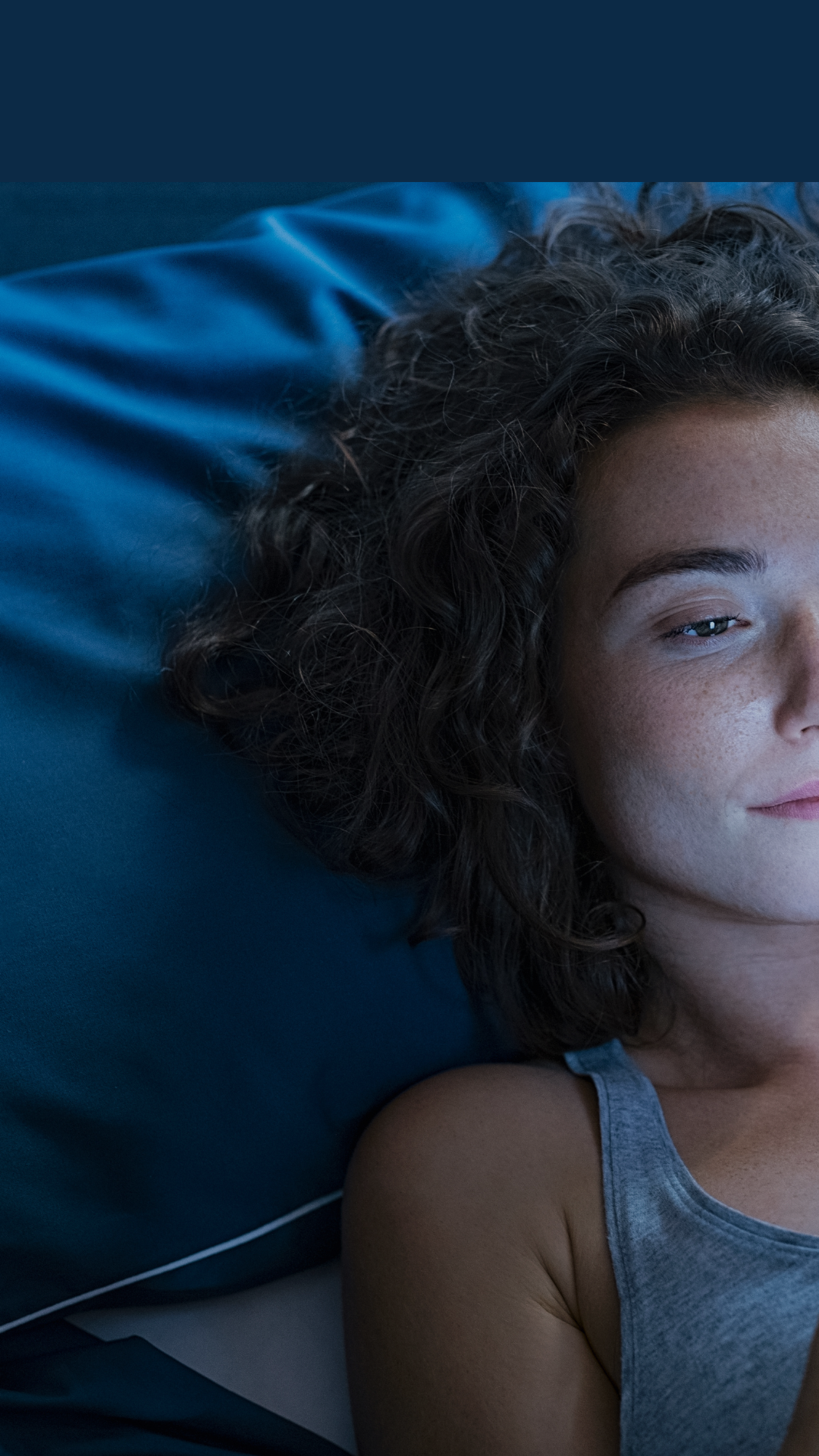 A woman struggling with insomnia stares at her smart phone in bed late at night