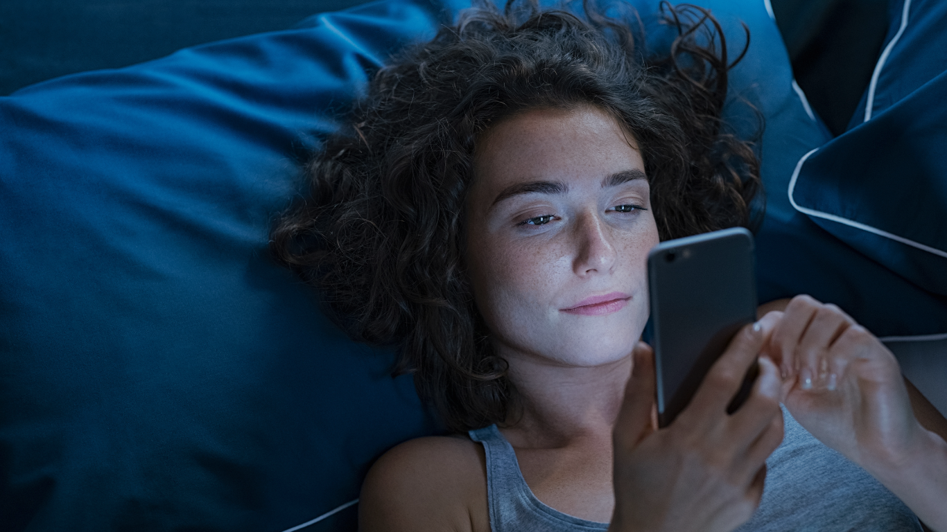 A woman struggling with insomnia stares at her smart phone in bed late at night