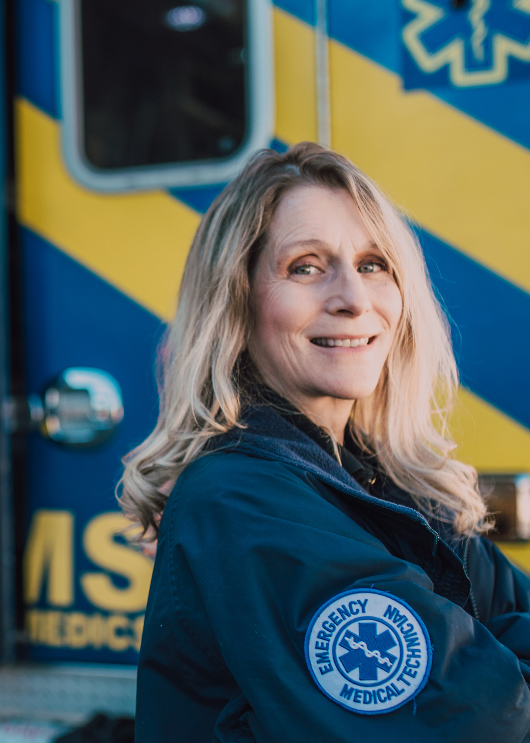 A EMS or EMT worker stands proudly next to her ambulance 