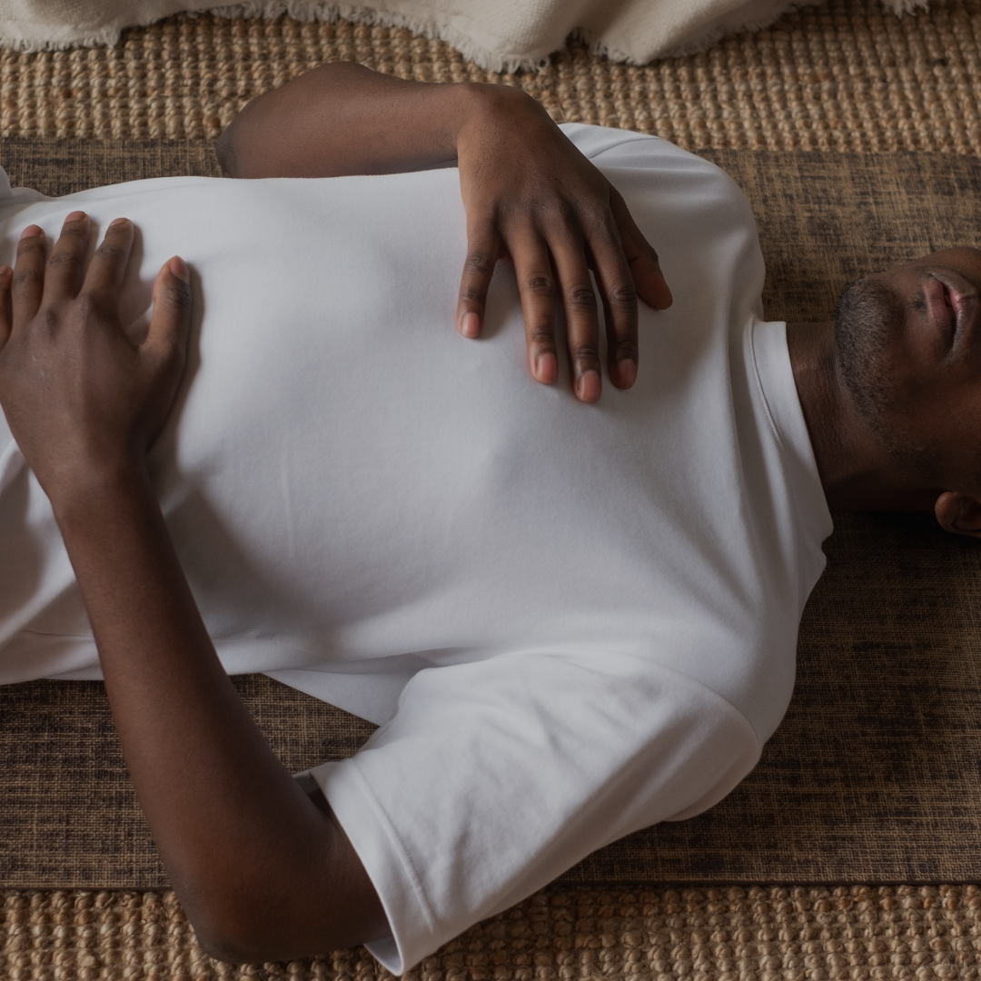 A man lays on the floor practicing deep breathing exercises with his hands over his chest