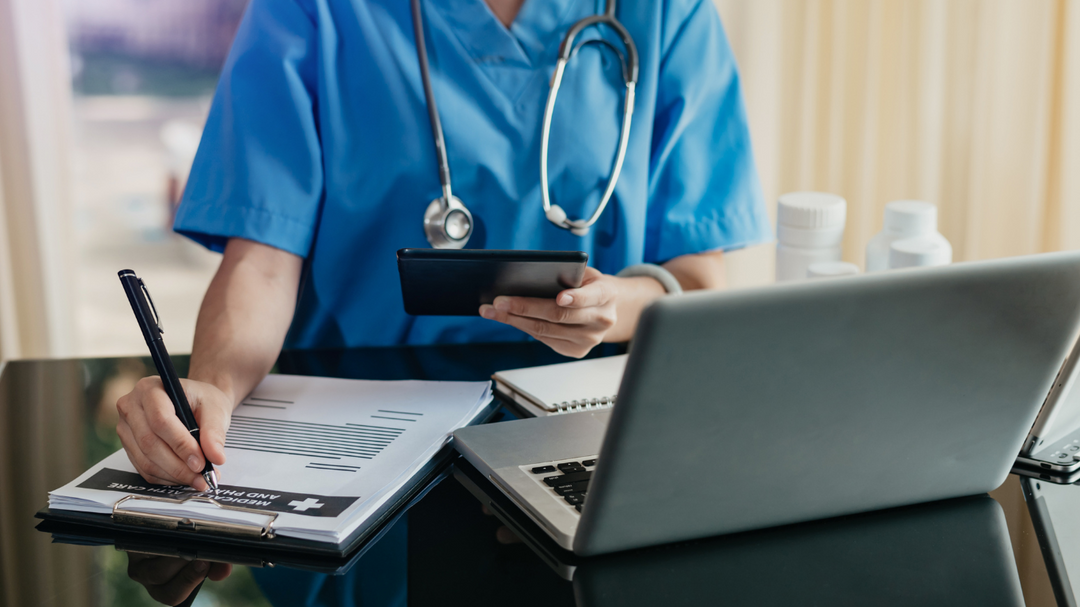 A doctor or nurse fills out paperwork at their desk